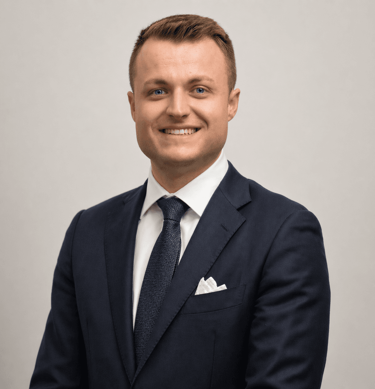 Professional headshot of a smiling man wearing a navy blue suit, white shirt, and tie.